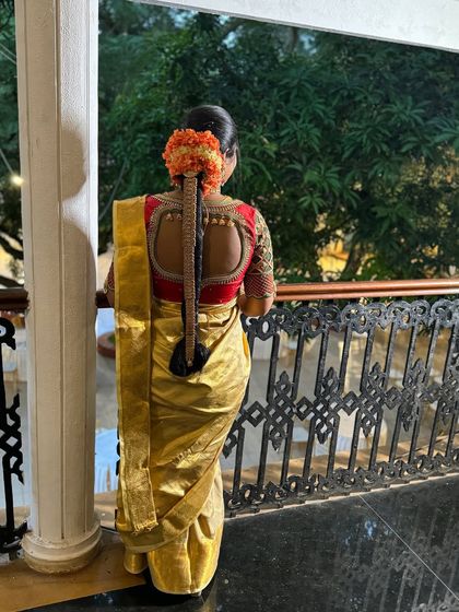 A view from the back, showcasing the elegant saree drape and the traditional long braid adorned with fresh flowers, a hallmark of South Indian bridal beauty.