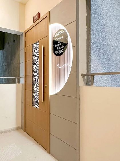 A beautiful main door design with a vertical glass insert and a large, modern handle. The adjacent wall features a custom backlit nameplate, creating a cohesive and stylish entrance.