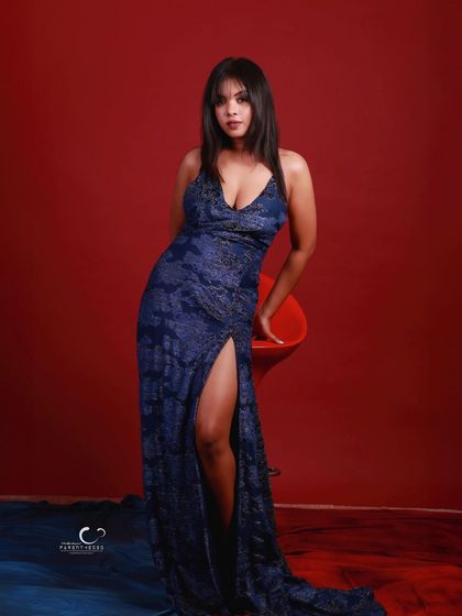 A confident and alluring pose leaning against a red stool. The composition highlights the elegant lines of the gown.