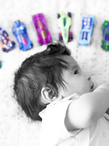 A creative shot using selective color to highlight the bright toy cars. This artistic approach adds a unique touch to this baby boy's milestone photos.