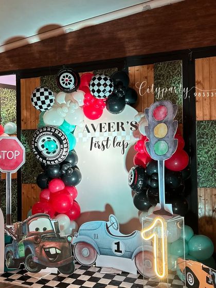 A complete view of the 'Aveer's First Lap' car-themed birthday party, showing the checkered floor, traffic light prop, and custom backdrop.