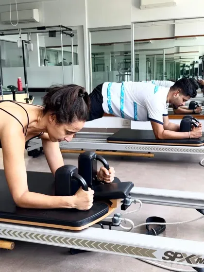 Namrata Purohit and Shreyas Iyer hold a synchronized plank on the reformer. This demonstrates the core strength and endurance that Pilates builds, which is the foundation of all athletic movement.