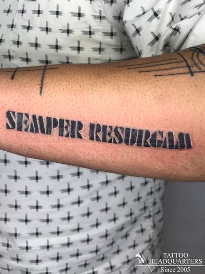 A bold, block-letter tattoo of the Latin phrase "SEMPER RESURGAM," meaning "I will always rise again."