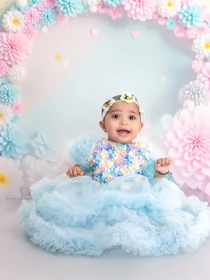 A dreamy pastel rainbow theme perfect for a baby girl's photoshoot. The setup features a beautiful arch of handmade paper flowers in pink and blue, creating a soft, ethereal look.