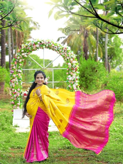 A beautiful outdoor portrait of a mother-to-be in a yellow and pink saree, with the fabric flowing in the wind.