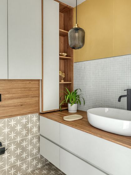 The bathroom design combines clean lines with a playful mix of textures. A soft yellow accent wall and mosaic backsplash bring brightness, while patterned floor tiles add character and visual depth.