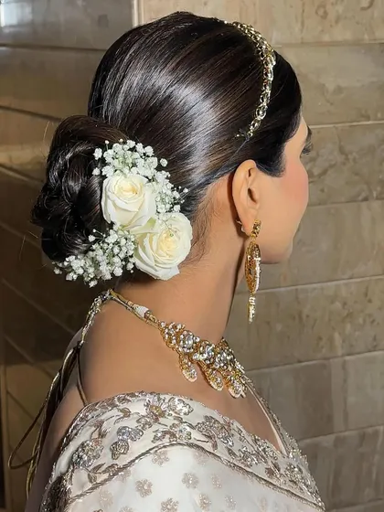 A messy bun styled with white roses and baby's breath for a soft, romantic feel. This is a versatile look that works for both weddings and receptions.