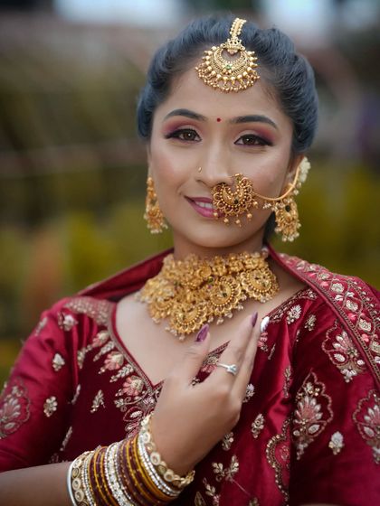 A close-up of a beautiful North Indian bridal look. The focus is on the intricate gold jewellery, including the nath and maang tikka, paired with warm, glowing makeup.