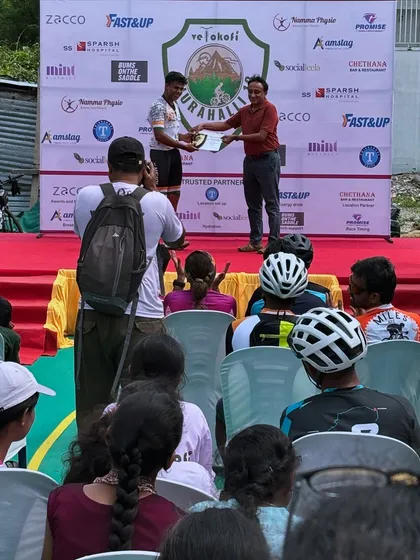 A podium moment at the Turahalli 13 race. One of the participants receives their award, with the crowd of fellow cyclists cheering them on.
