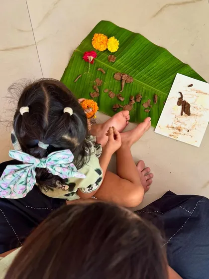 A child sits with her creation, a piece of art made with mud and flowers on a banana leaf. This showcases how we use various natural canvases in our workshops.