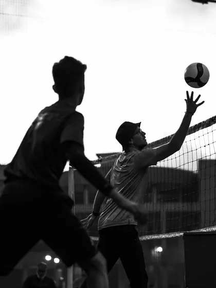 Two players at the net, one setting the ball just out of reach. A dramatic black and white capture of the game's flow.