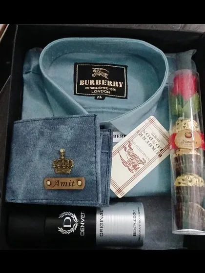 A stylish gift box containing a personalized denim wallet, a branded shirt, deodorant, and a tube of chocolates with a rose.