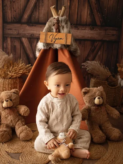 A happy one-year-old boy playing with a teddy bear during his camp-themed birthday photoshoot.
