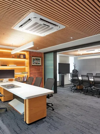 This executive office suite features a large desk, an integrated meeting table, and extensive back-lit shelving. A sliding glass wall can separate the personal office from the meeting area.