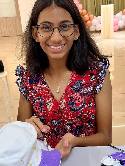 A young girl smiles while painting a custom design on her bucket hat at a birthday celebration.