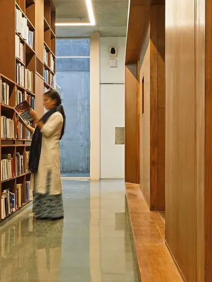 A student browses the collection in a quiet aisle of the Lilavati Lalbhai Library. The integration of structure and shelving, along with warm, indirect lighting, creates an environment conducive to focused study and research.