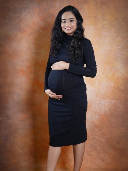 A simple and beautiful solo portrait of the mother-to-be. Dressed in a comfortable black fitted dress against a warm backdrop, her radiant smile is the focus.