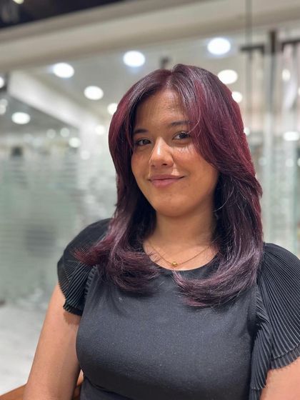 A happy client showing off her new red wine hair color. The shade is rich and vibrant, and the layered cut gives her hair beautiful shape and movement.