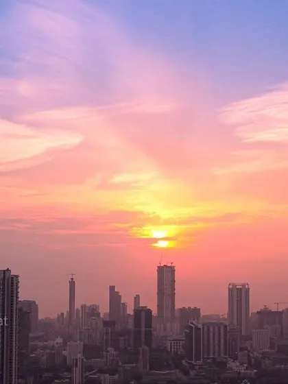 The Mumbai skyline is captured under a beautiful sunset, with the sky filled with pink and orange hues and wispy clouds.
