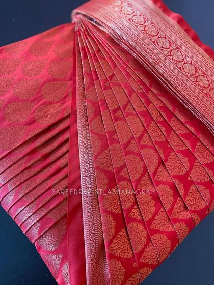 A close-up of a red silk saree with gold motifs, expertly box-folded to protect the fabric and design.