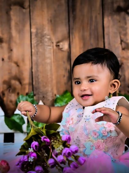 A baby girl in a pastel dress holding a flower.