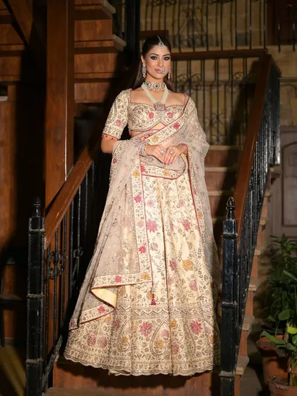 A full-length portrait on a staircase, showcasing the grandeur of the ivory lehenga. The bride looks poised and elegant, ready for her grand event.