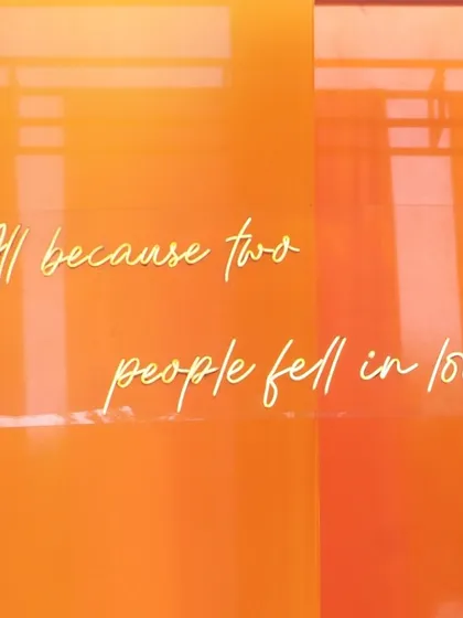 A neon sign with the quote "All because two people fell in love" set against a vibrant orange backdrop, adding a touch of modern romance.