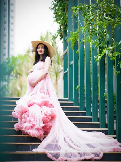 A breathtaking outdoor maternity portrait. The expecting mother stands on a staircase in a magnificent pink ruffled gown, creating a dramatic and elegant image.