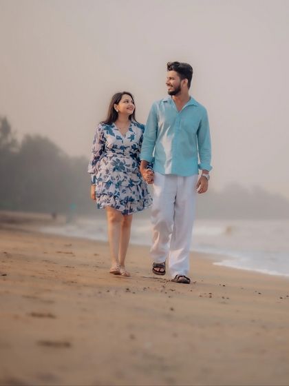 A classic romantic walk on the beach. The couple holds hands and looks at each other, their connection evident as they stroll along the sand during their pre-wedding shoot.