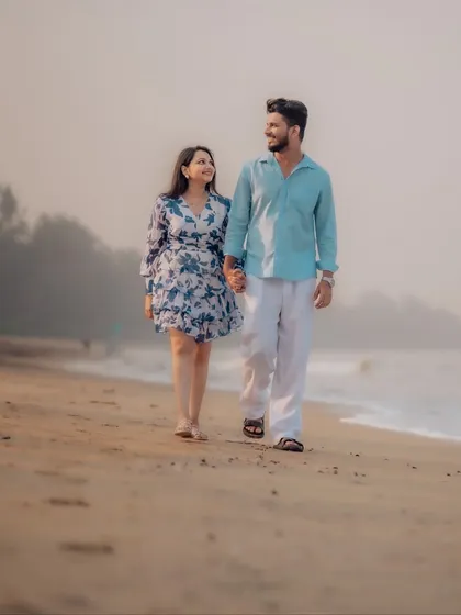 A classic romantic walk on the beach. The couple holds hands and looks at each other, their connection evident as they stroll along the sand during their pre-wedding shoot.