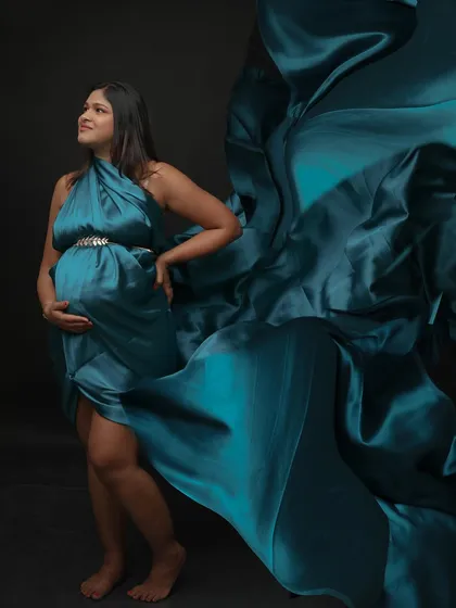 A powerful and dramatic portrait with a flowing teal satin drape. The mom-to-be looks up with a hopeful expression, embodying the journey of motherhood.