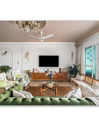 A cozy and eclectic living room featuring a green chesterfield sofa and floral armchairs. The space is filled with personal touches and textures, from the jute rug to the curated items on the TV console.