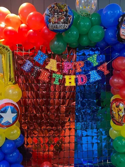 A colorful Avengers-themed birthday decoration with a shimmer wall backdrop and balloon columns representing different heroes.