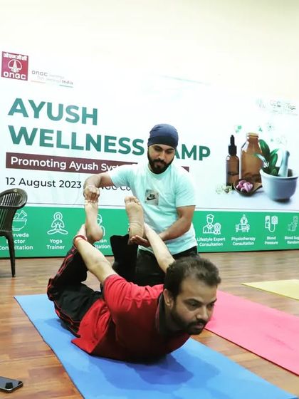 I am providing a hands-on assist for Dhanurasana (Bow Pose) during an Ayush Wellness Camp at ONGC. Yoga therapy is a key part of my corporate offerings.