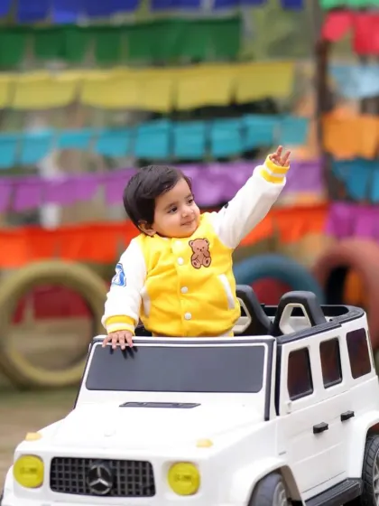 A cheerful wave from a little boy in his toy car. The colorful flags in the background add a festive and playful touch to this outdoor photo.