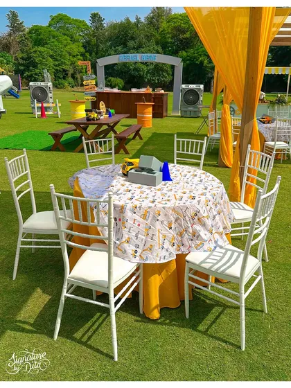 A round dining table setup for the construction party, featuring themed linens and surrounded by classic white Chiavari chairs.