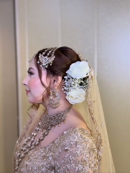 A side profile of the bride, showcasing her elegant updo with fresh white roses. The makeup is soft and sophisticated.
