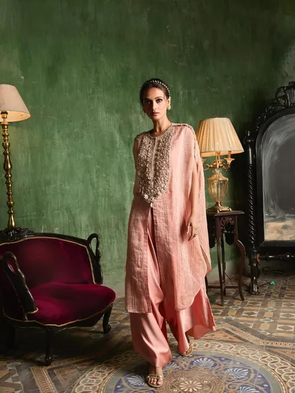 A model walks in a beautiful pink layered ensemble with a heavily beaded yoke, showcasing its movement and grace.