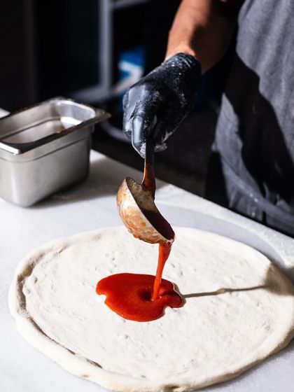 It all starts with the sauce. A ladle of rich, red tomato sauce is poured onto the stretched pizza dough, the first layer of flavour.