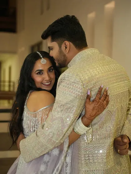 A sweet and romantic pose, with the groom-to-be embracing his fiancée from behind as she smiles at the camera.