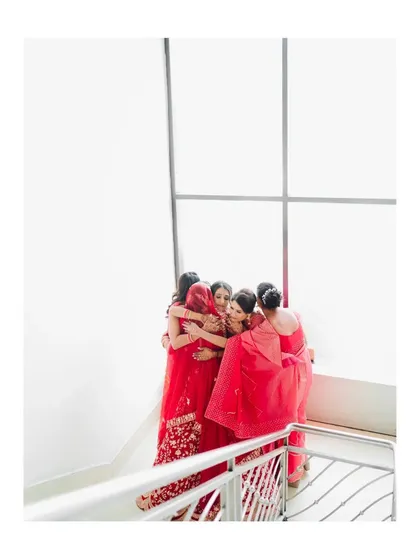 An emotional moment as the bride shares a group hug with her bridesmaids, all dressed in shades of red and pink.