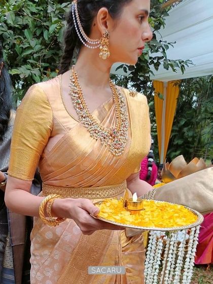 Our client Madhuri at a wedding, wearing a custom backless blouse with monotone gold embroidery and a matching belt to complement her gold Kanjeevaram saree.