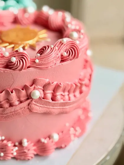 A detailed shot of the sun side of the cosmic cake, with its pink piping, edible pearls, and golden sun.