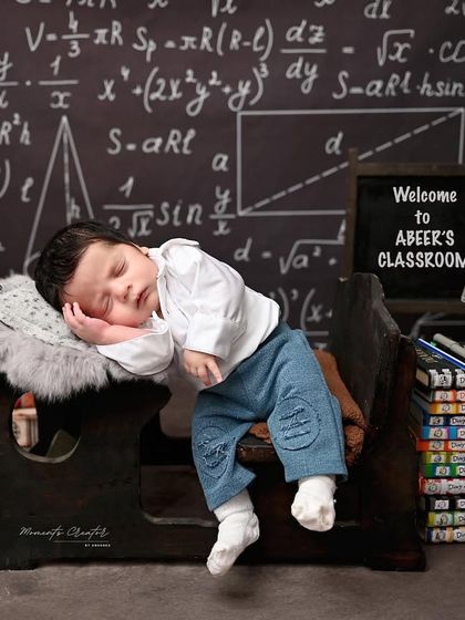 Back to school, but in dreamland. This one-month-old 'little professor' is napping at his desk in a fun, classroom-themed setup.