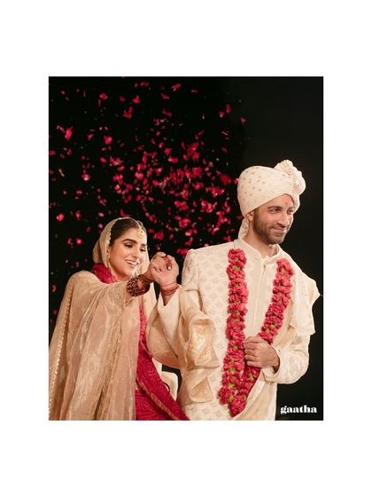 A beautiful shot of the couple during their Varmala, with rose petals showering down against a dark background.