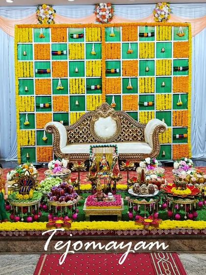 A baby shower setup featuring a colorful marigold backdrop and an ornate throne, complemented by a full display of traditional offering plates.