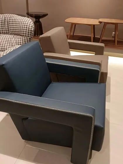 A modern and minimalist sofa chair available in deep blue and beige leatherette. The exposed stitching and clean, boxy frame make it a great fit for contemporary interiors.