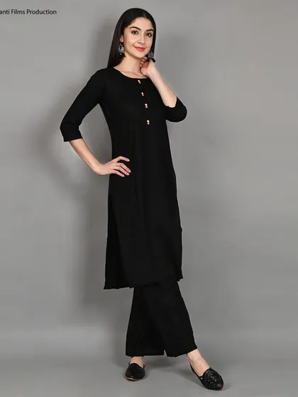 A classic three-quarter pose for a simple black kurti and palazzo set. This shot is a staple for e-commerce, providing a clear and flattering view of the outfit on a neutral grey background.