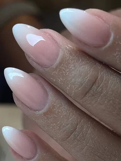A close-up of a flawless ombré manicure on almond-shaped extensions. The blend between the pink and white is perfectly seamless.