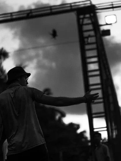 A player watches the ball he just served, a silhouette against the evening sky.